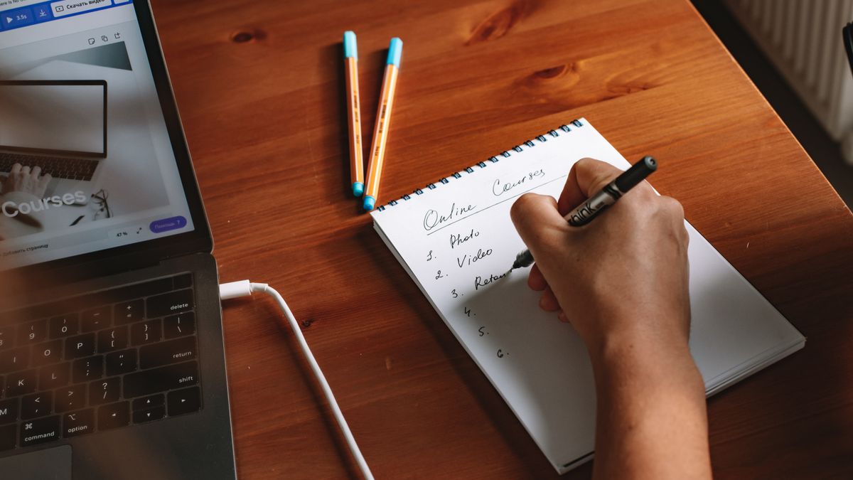 Photo of a person writing a list of online courses on a notepad next to a laptop.