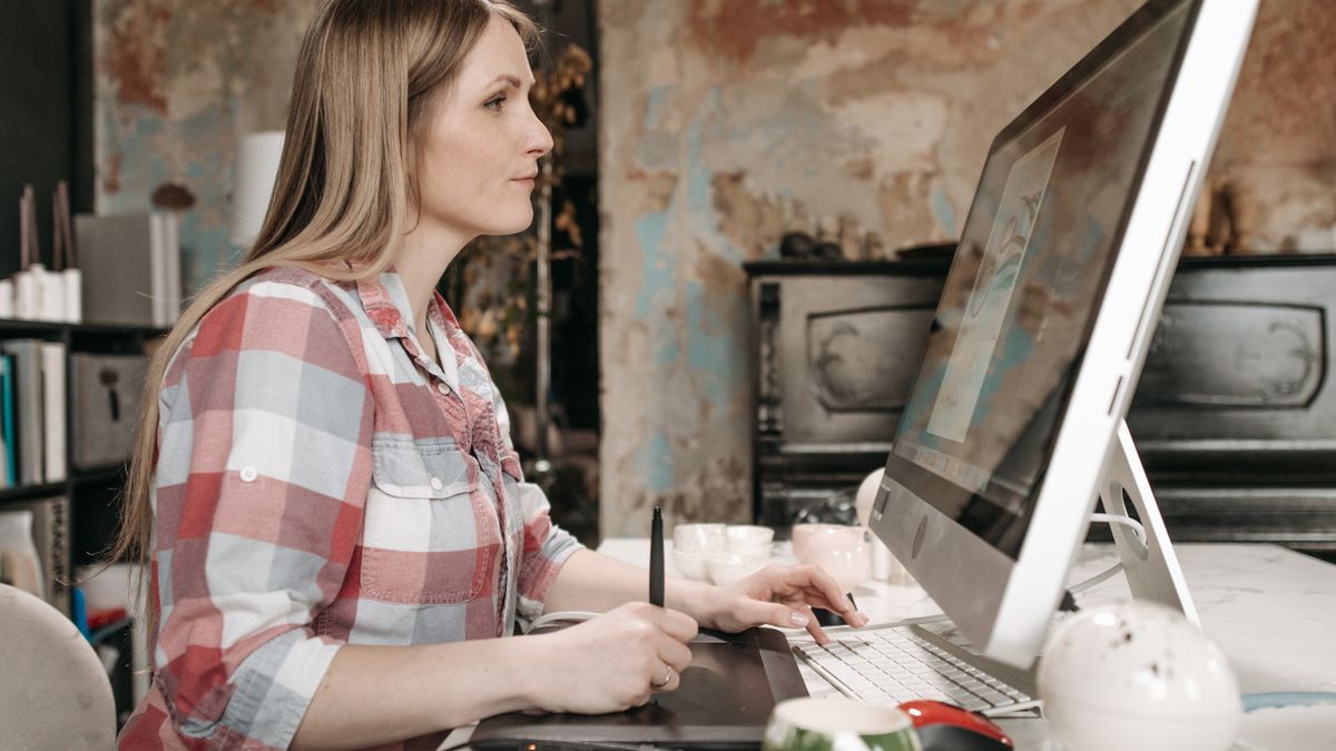 Side view of a woman using a graphics tablet at a computer in a stylish office space.