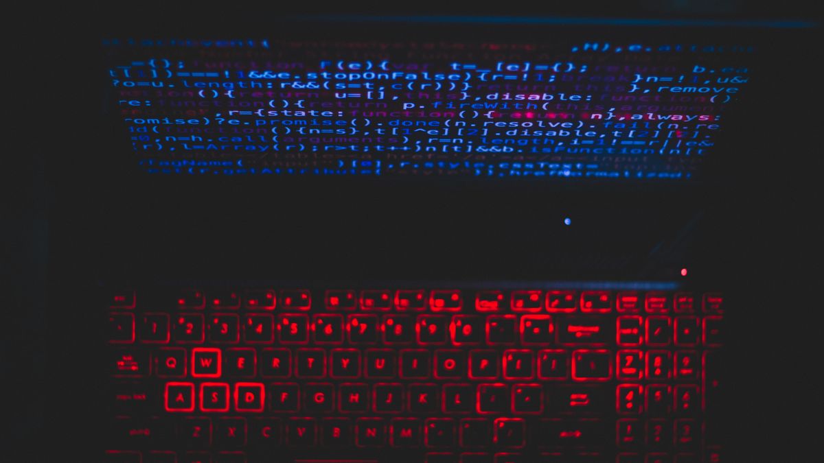 Dark-themed laptop setup with a red glowing keyboard and code on screen, ideal for tech enthusiasts.