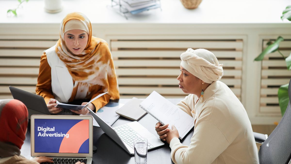 Three women in hijabs collaborating on digital advertising strategies around a table with laptops.