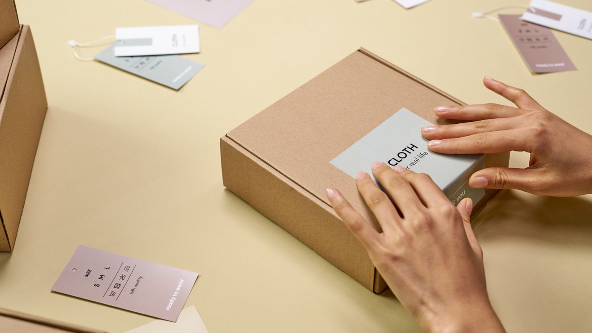 Hands carefully packing a cardboard box with multiple tags around, emphasizing sustainable packaging.