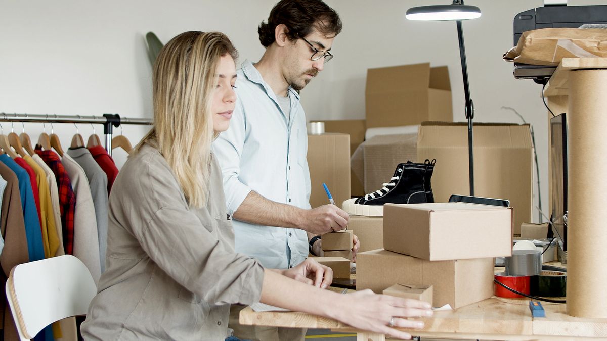 Business partners organizing inventory in an online store setup with clothes and boxes.