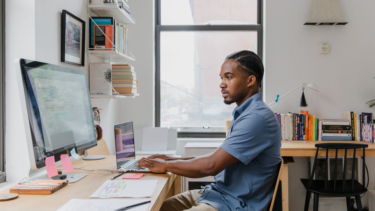 A professional man working on a laptop and computer in a stylish home office setting.