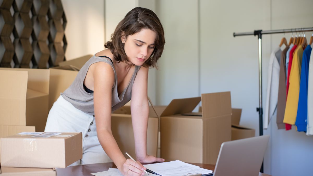 Young woman managing her online clothing business from home office with boxes and laptop.
