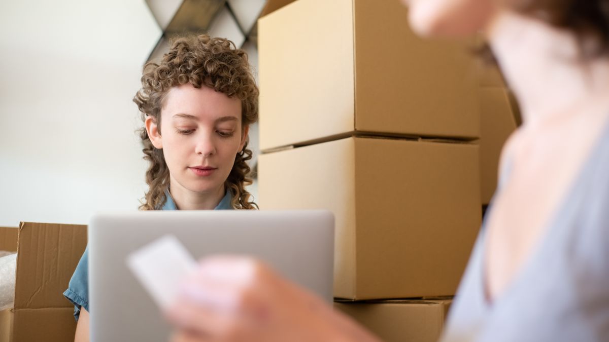 Women managing a small business surrounded by cardboard boxes and using a laptop for online orders.