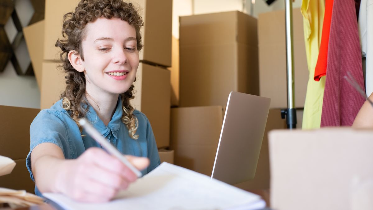 Smiling young woman managing a small business with laptop and packages around her.
