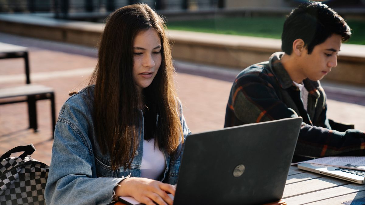 Two young adults working on laptops at an outdoor table.