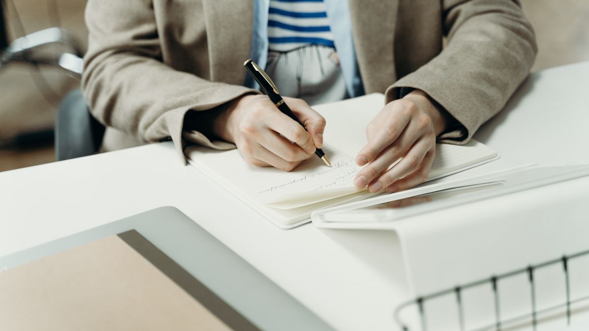 Close-up of an adult writing in a notebook at a modern office desk, capturing professional planning.