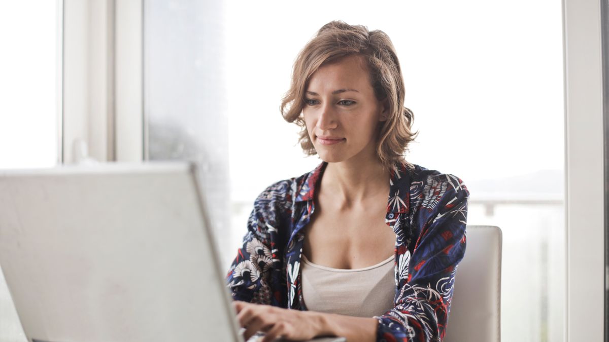 A woman typing on a laptop in a bright, modern home office setting.